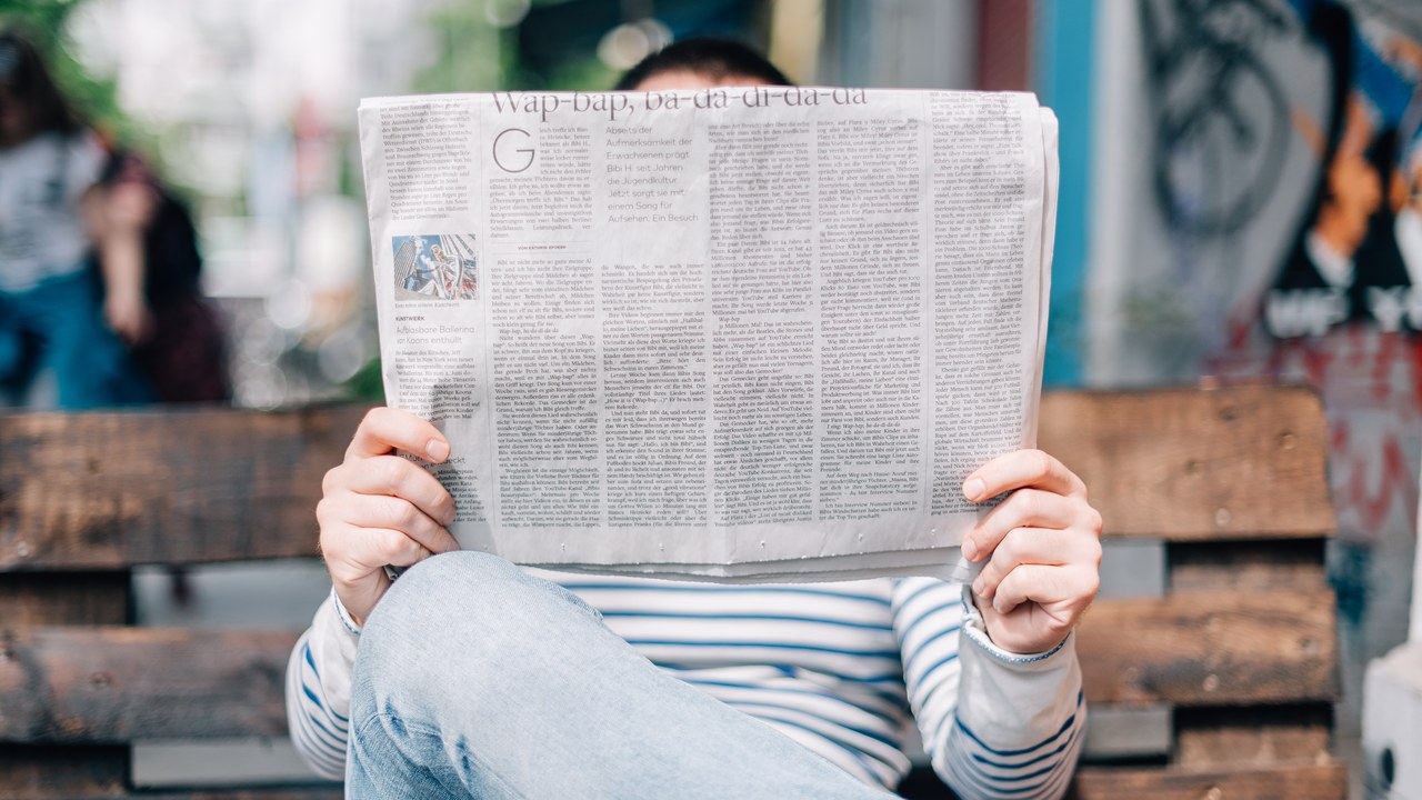 Person som läser en tidning på en bänk.